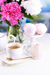 Composition of beautiful peonies in vase, tea in cup and