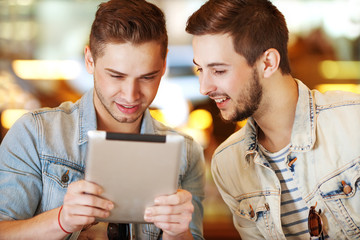 Two young men / students using tablet computer in cafe