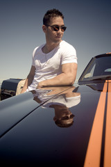 Young handsome guy standing by muscle car on road