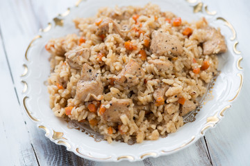 Pilaf with chicken on a glass plate over white wooden background