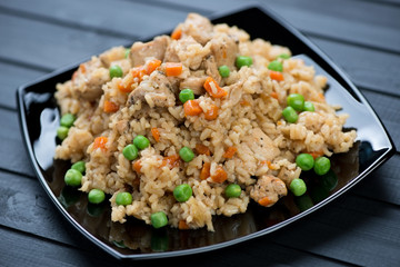 Pilaf with chicken on a glass plate over black wooden background