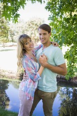 Fototapeta premium Loving young couple standing together in the park smiling at cam