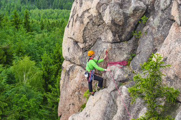 Man climbs a vertical wall of one of the rocks against forest