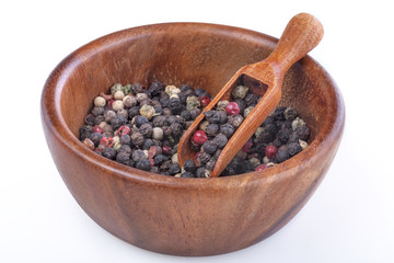 Peppercorns in bowl with a wooden spoon on a white