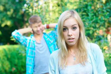 Sad girl with her boyfriend on the background at the park