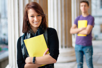 Smiling girl holding a notebook with a boy at the background