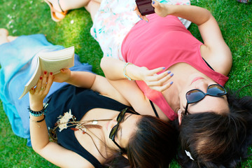 Two asian girl lying on a grass with a book and a phone