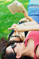 Two asian girl lying on a grass with a book and a phone