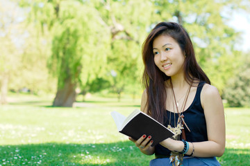 Fototapeta premium Smiling asian girl reading a book at the park