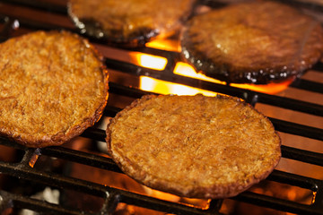 Hamburger patties on a grill with fire under