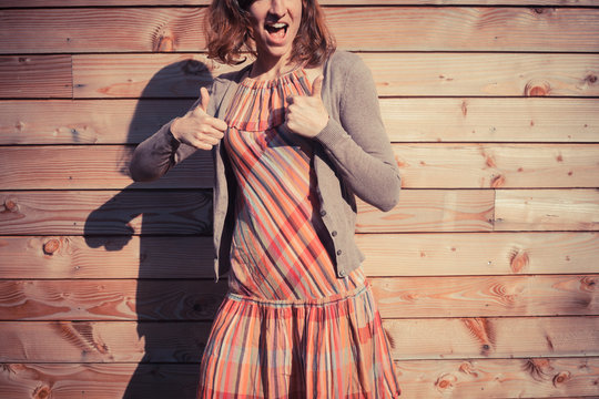 Young woman giving thumbs up outside wooden cabin