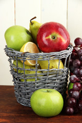 Different fruits in basket on table on wooden background