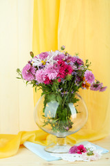 Wildflowers in glass vase on table on yellow fabric background