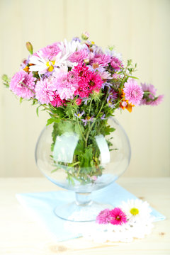 Wildflowers in glass vase on table on light background