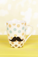 Cup with mustache on table on light background