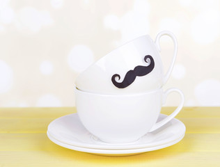 Cup with mustache on table on light background