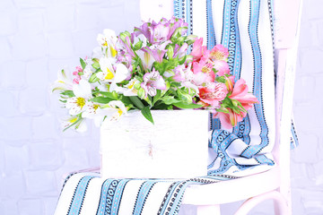 Beautiful bouquet of freesias in wooden box on chair in room