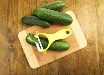 Peeler and cucumbers on wooden table