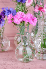 Beautiful summer flowers in vases on pink wooden background
