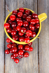 Sweet cherries in mug on wooden background