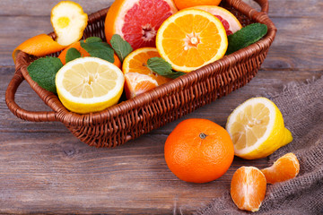 Obraz na płótnie Canvas Fresh citrus fruits with green leaves in wicker basket