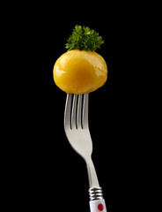 Young boiled potato on fork on black background
