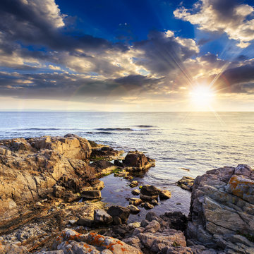 calm sea with boulders on coast at sunset