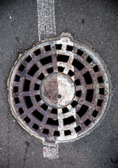 Manhole with metal cover in asphalt with white road marking line