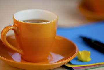 Orange coffee cup on brown writing paper with pen