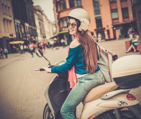 Young cheerful girl driving scooter in in european city