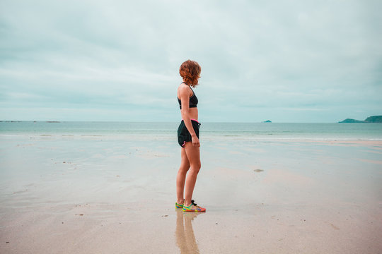 Young woman in workout clothes standing on beach