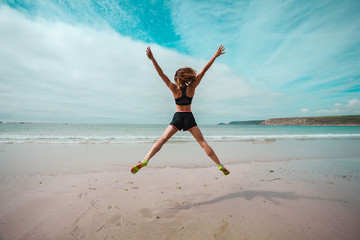 Young woman doing star jumps on the beach - 65969230