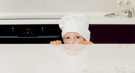 Child in a chefs toque hiding behind a counter