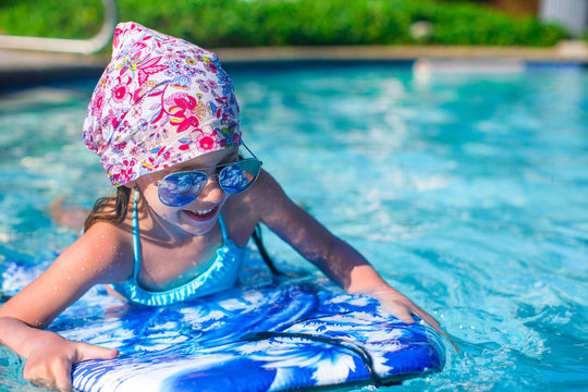 Little girl swimming on a surfboard in swimmingpoll