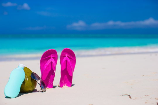 Flip flops, coconut and suncream on white sand