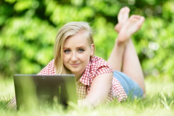 Young attractive woman lying on lawn with laptop.