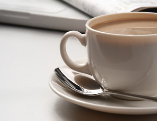 cup of coffee near the laptop and newspapers