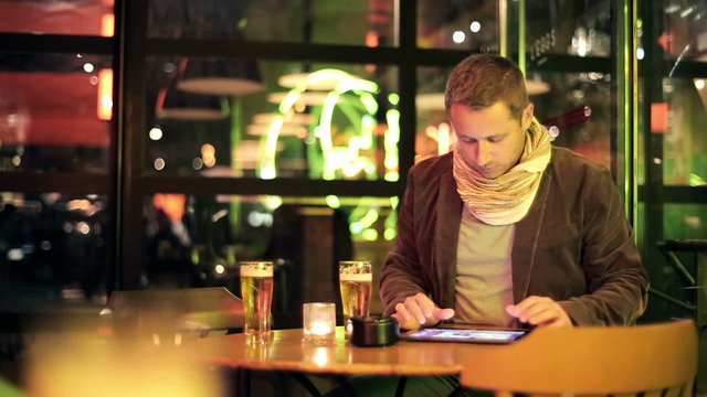 Young man watching photos on tablet computer and drinking beer