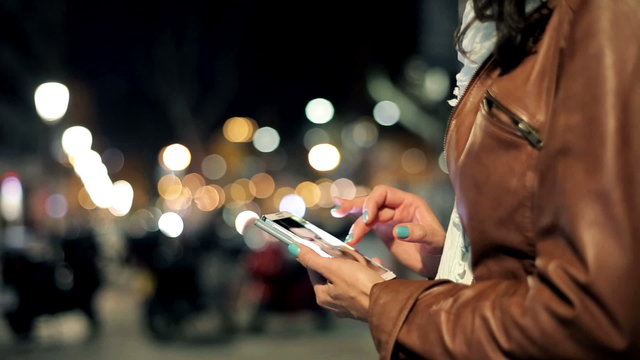 Woman watching photos on smartphone late at night in the city