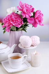 Composition of beautiful peonies in vase, tea in cup and