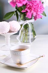 Composition of beautiful peonies in vase, tea in cup and