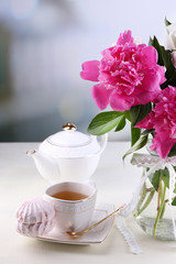 Composition of beautiful peonies in vase, tea in cup and