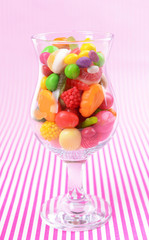Different colorful fruit candy in glass on pink background