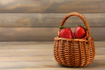 Red ripe strawberries in wicker basket on wooden background