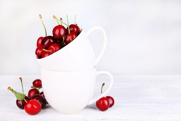 Ripe sweet cherries in cup on wooden table