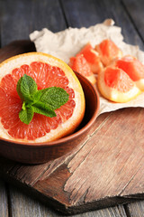 Part of ripe grapefruit in bowl, on wooden background
