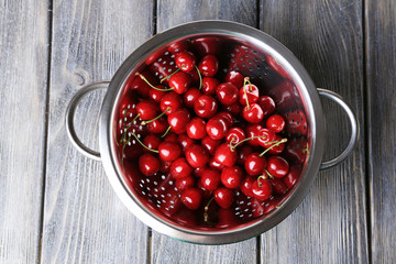 Sweet cherries in colander on color wooden background