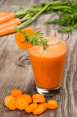 Carrot juice and carrot segments on a wooden background