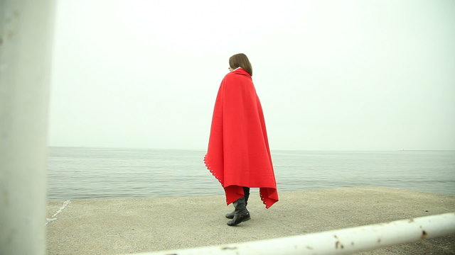 Lonely sad girl in red blanket on the sea shore