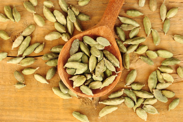 green cardamom in wooden spoon on wooden background close-up